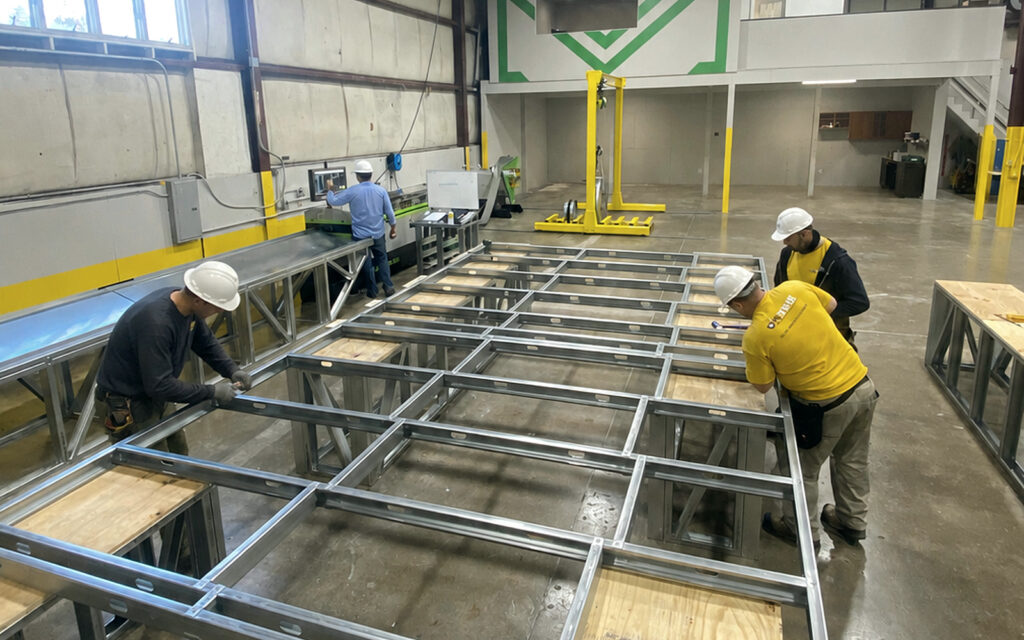 Shop crew assembling a cold-formed steel wall panel frame next to fabrication equipment